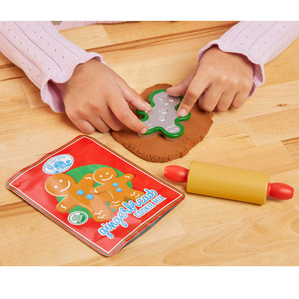 Child's hands using a gingerbread man cookie cutter on dough with a cookie book and rolling pin on a wooden table.